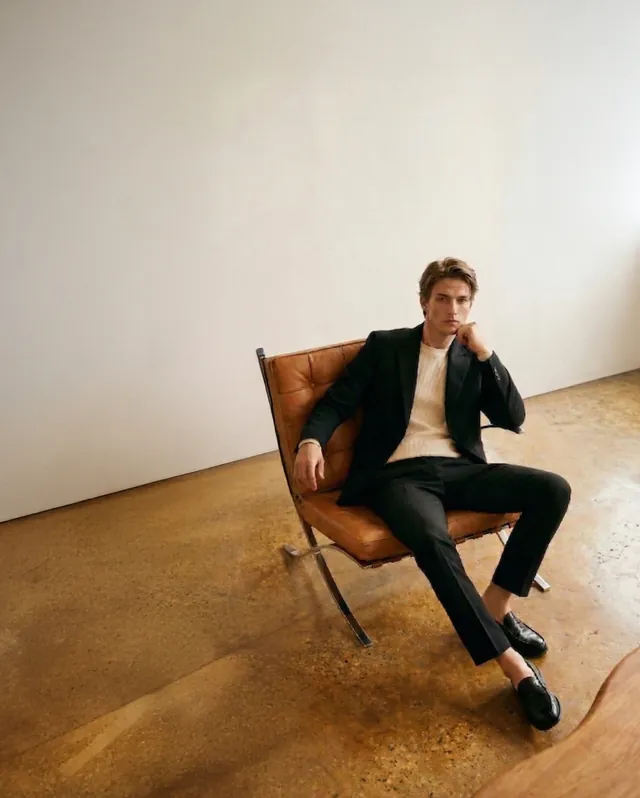 A model seated in a leather chair against a soft studio backdrop.