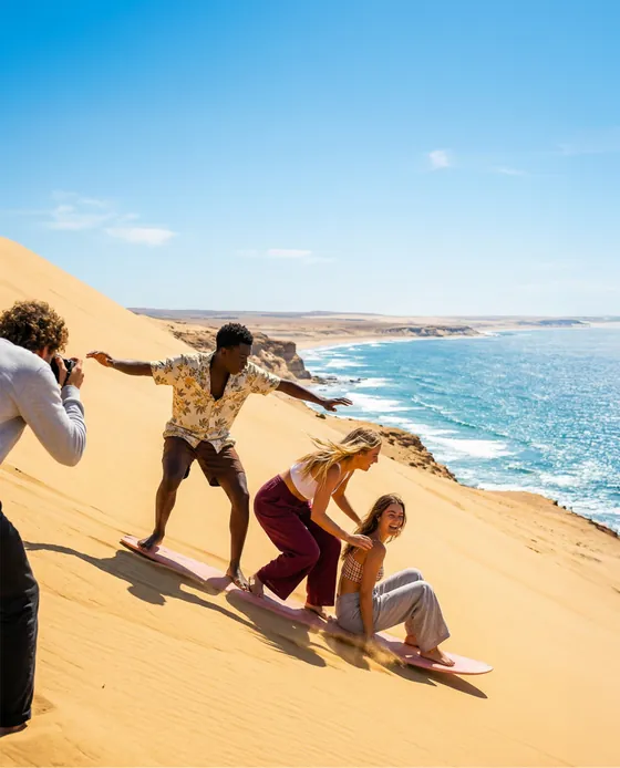 Sandboarders on a coastal dune, shot in bright daylight.